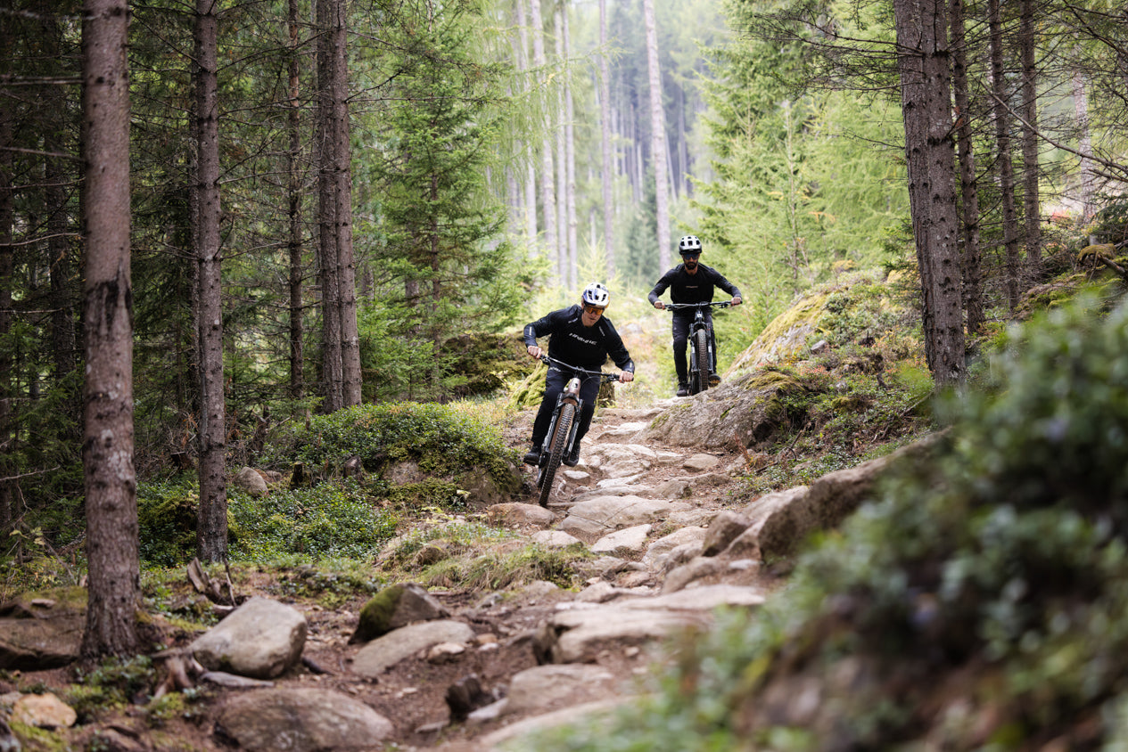 Two riders on Haibike eBikes navigating a steep, rocky mountain trail in the forest.