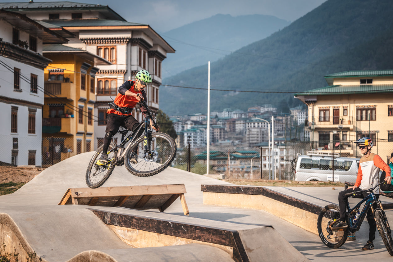 Haibike e-mountain bike riders performing jumps at pump track in Bhutan with Himalayan city and mountains backdrop adventure cycling 2025