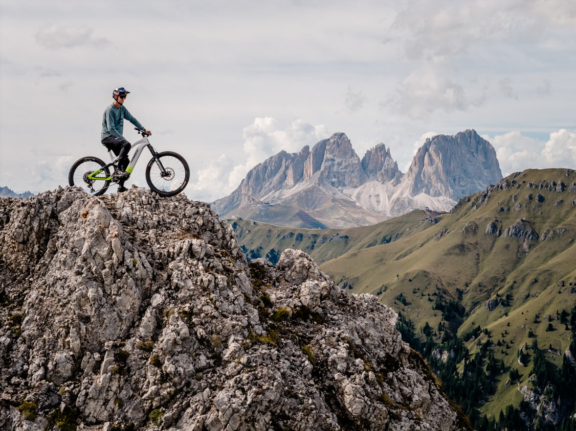 Rider with Haibike HYBE MY26 full-suspension e-mountain bike on a rocky Alpine summit with panoramic Dolomite mountain views – e-MTB adventure riding at altitude