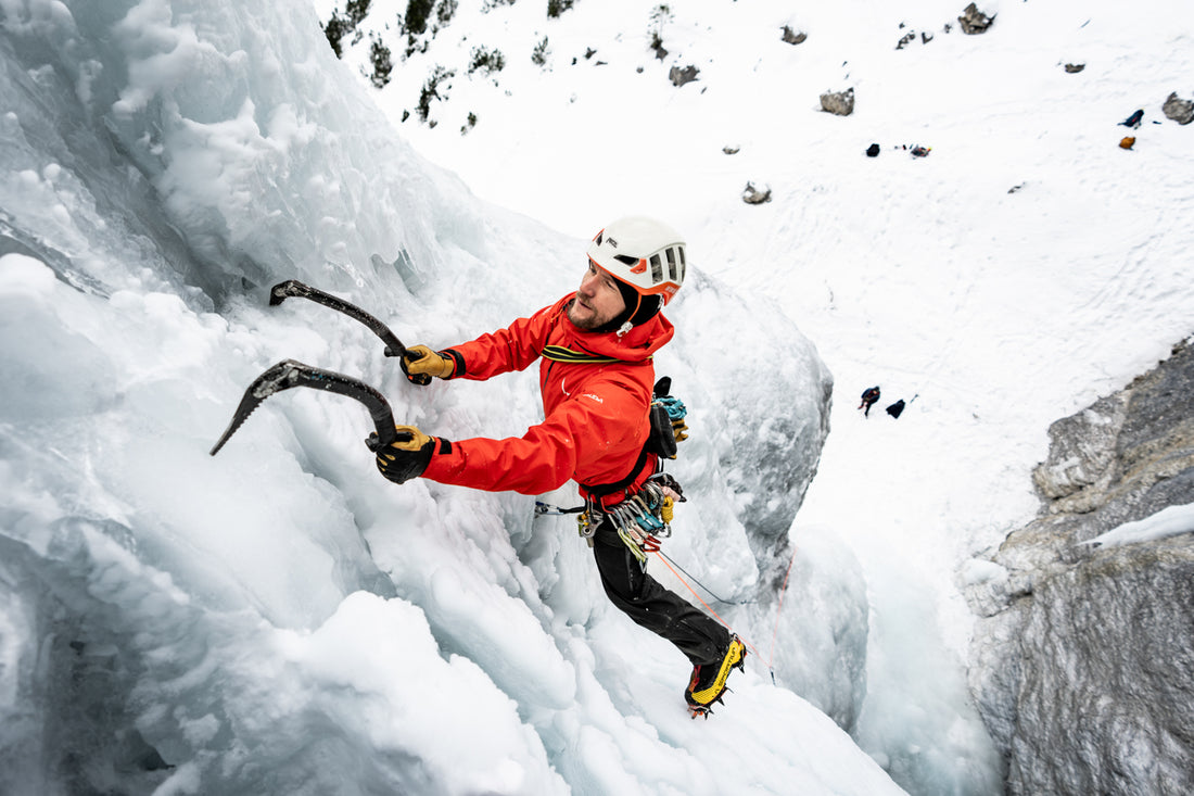 Ice climber in red jacket using ice axes on frozen waterfall during Stefan Voitl ice climbing tour in alpine winter