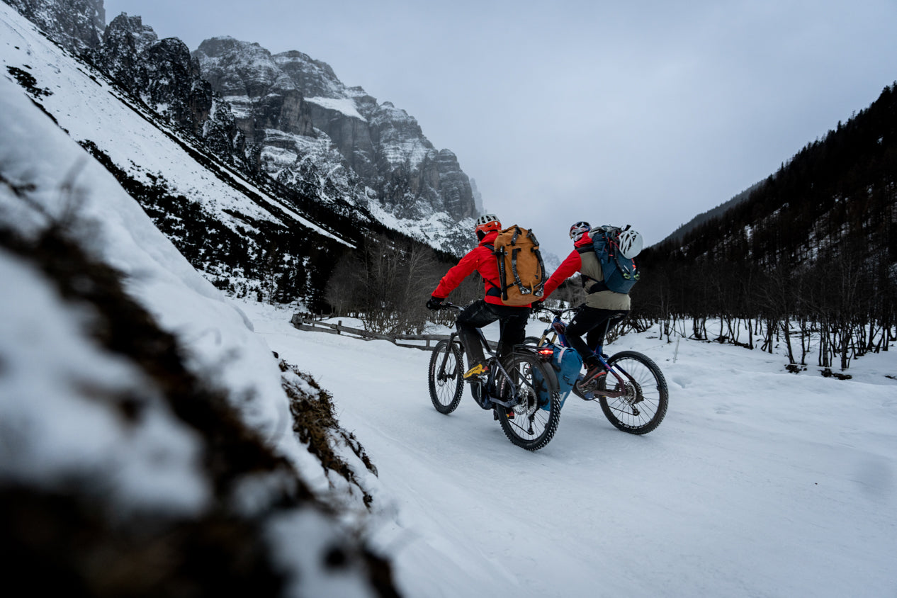 Two cyclists with backpacks riding Haibike e-bikes through snowy winter mountain valley Stefan Voitl ice climbing adventure tour