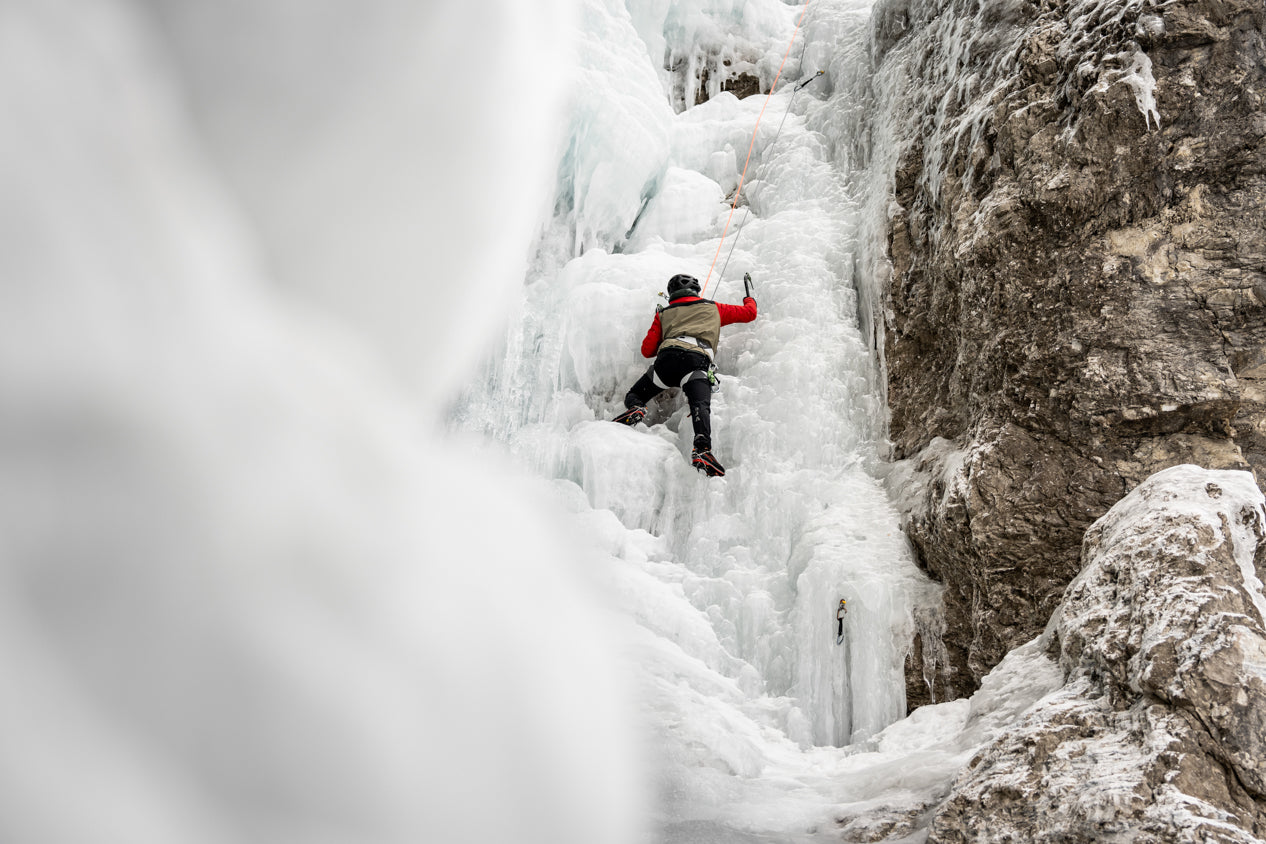 Ice climber ascending frozen waterfall on Stefan Voitl guided alpine ice climbing tour in winter mountains
